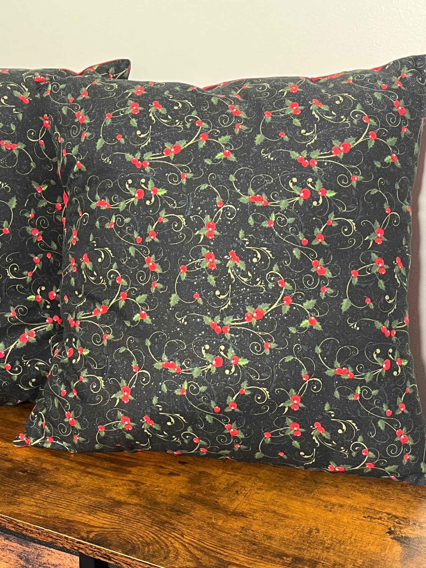 Christmas holly glitter pillow on black background with red backing displayed on wooden shelf