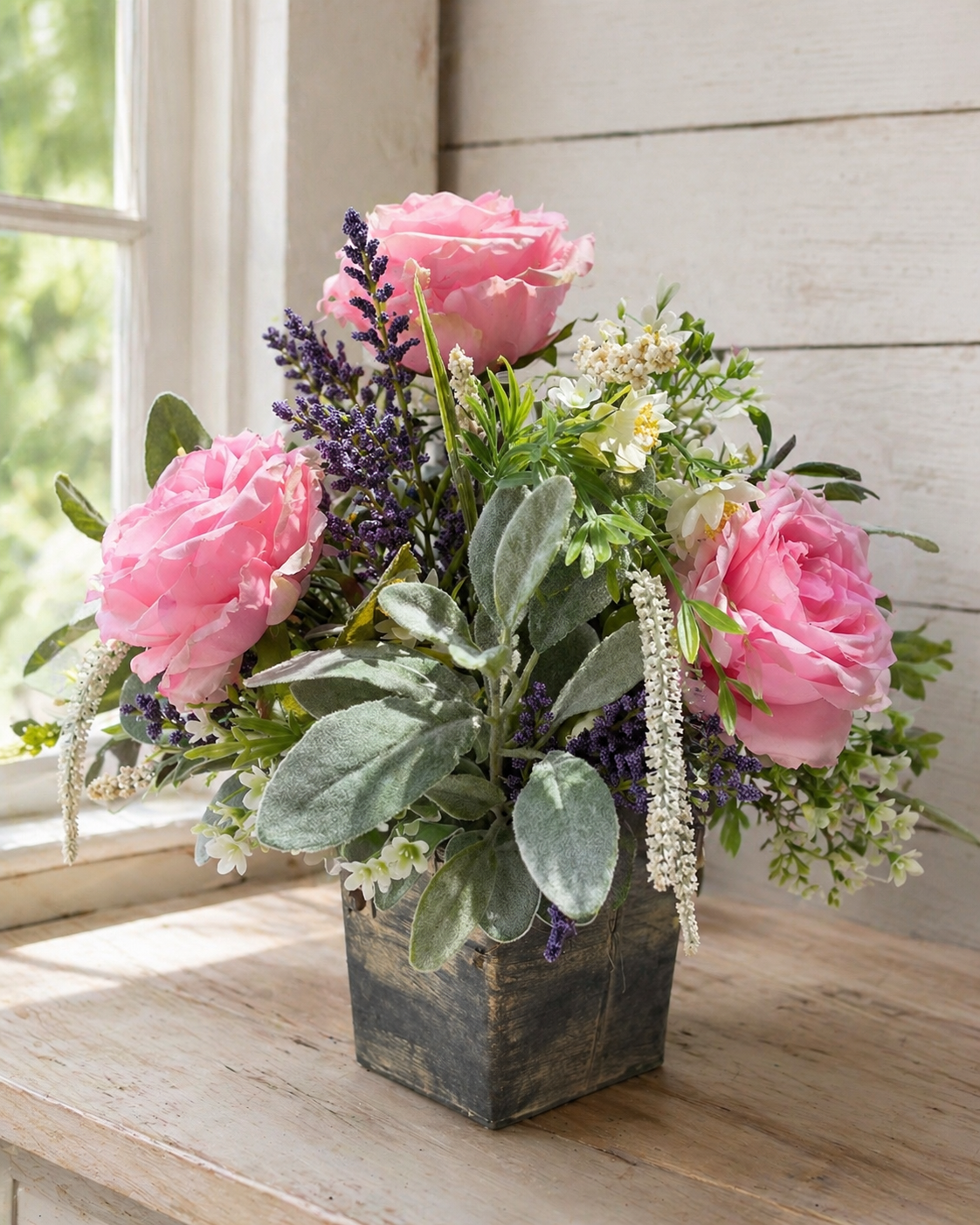 Floral arrangement with pink flowers and greenery in a wooden box on a wooden surface.