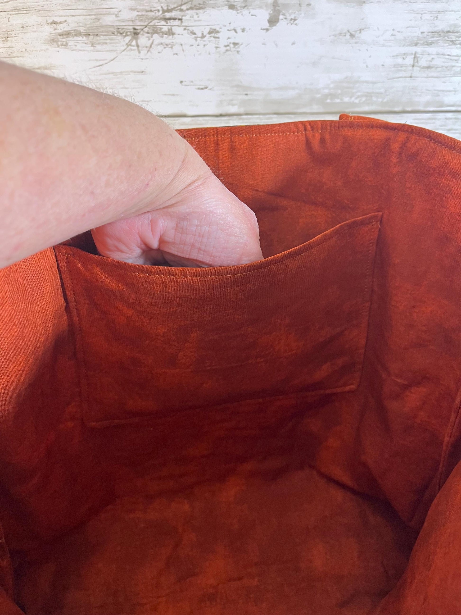 Close-up of a hand reaching into a red fabric bag with a wooden surface in the background.