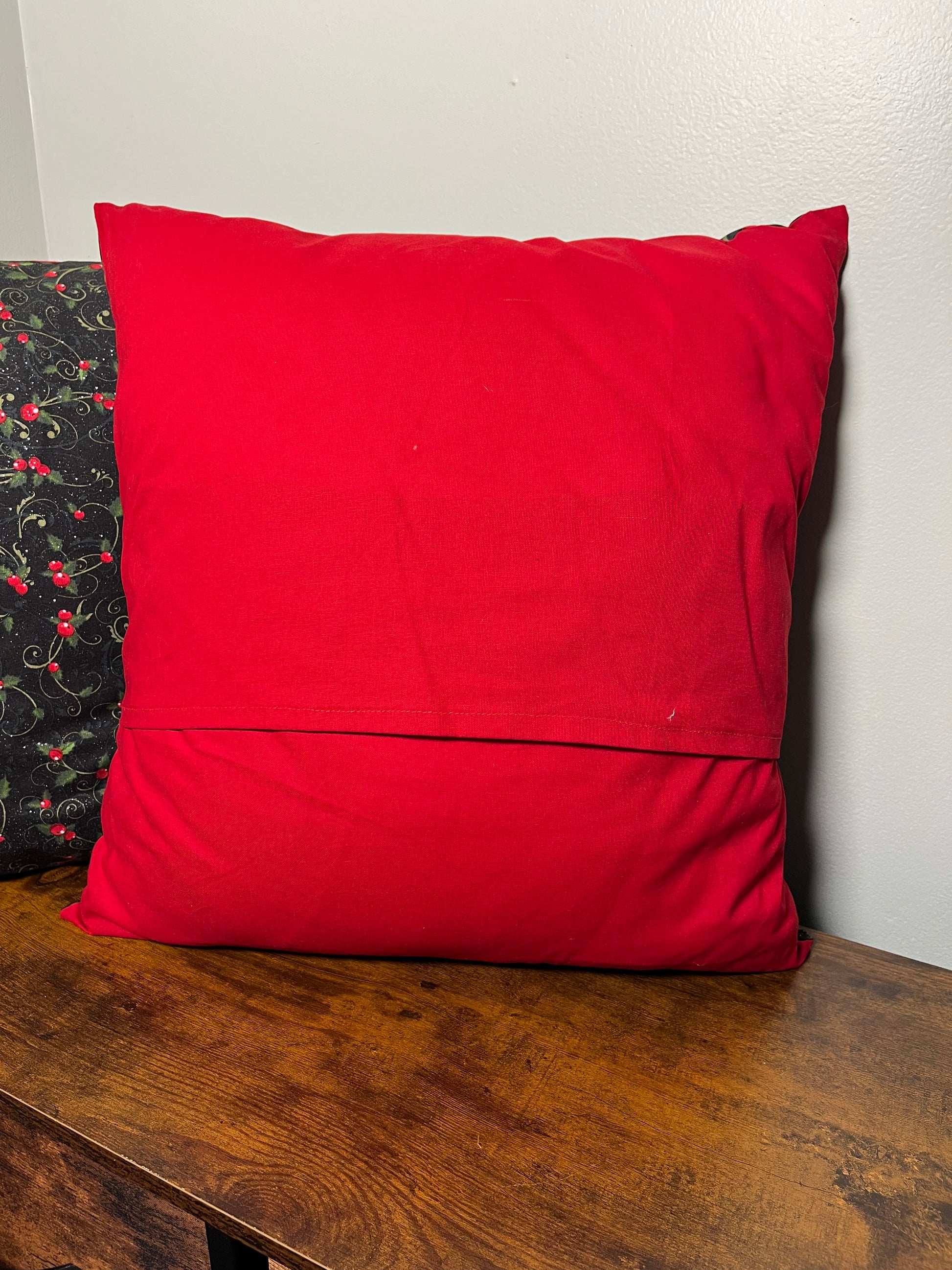 Red backing on holly pillow on a wooden surface with a grey wall background