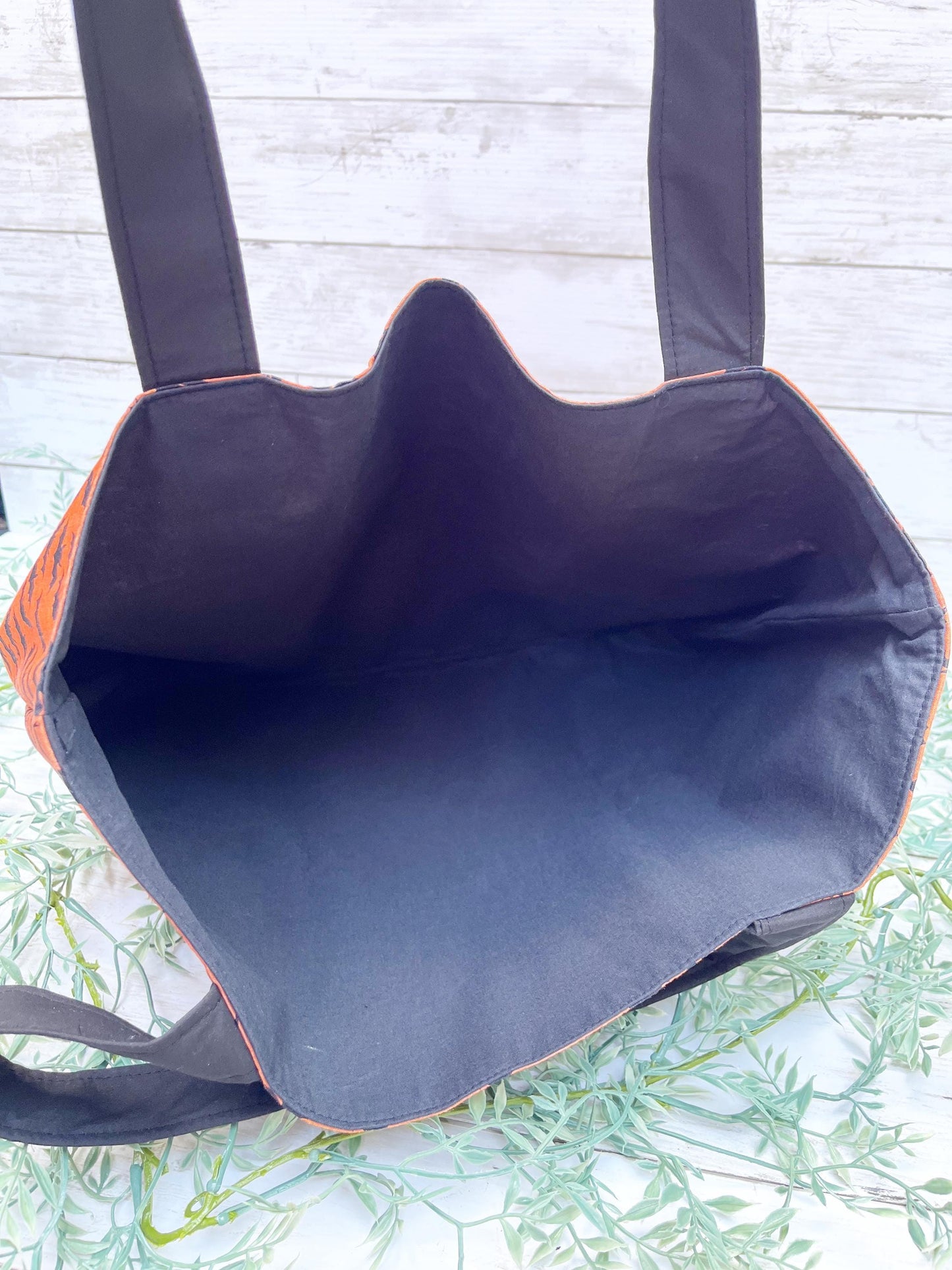Black tote bag with black  interior lining on a light wooden surface.