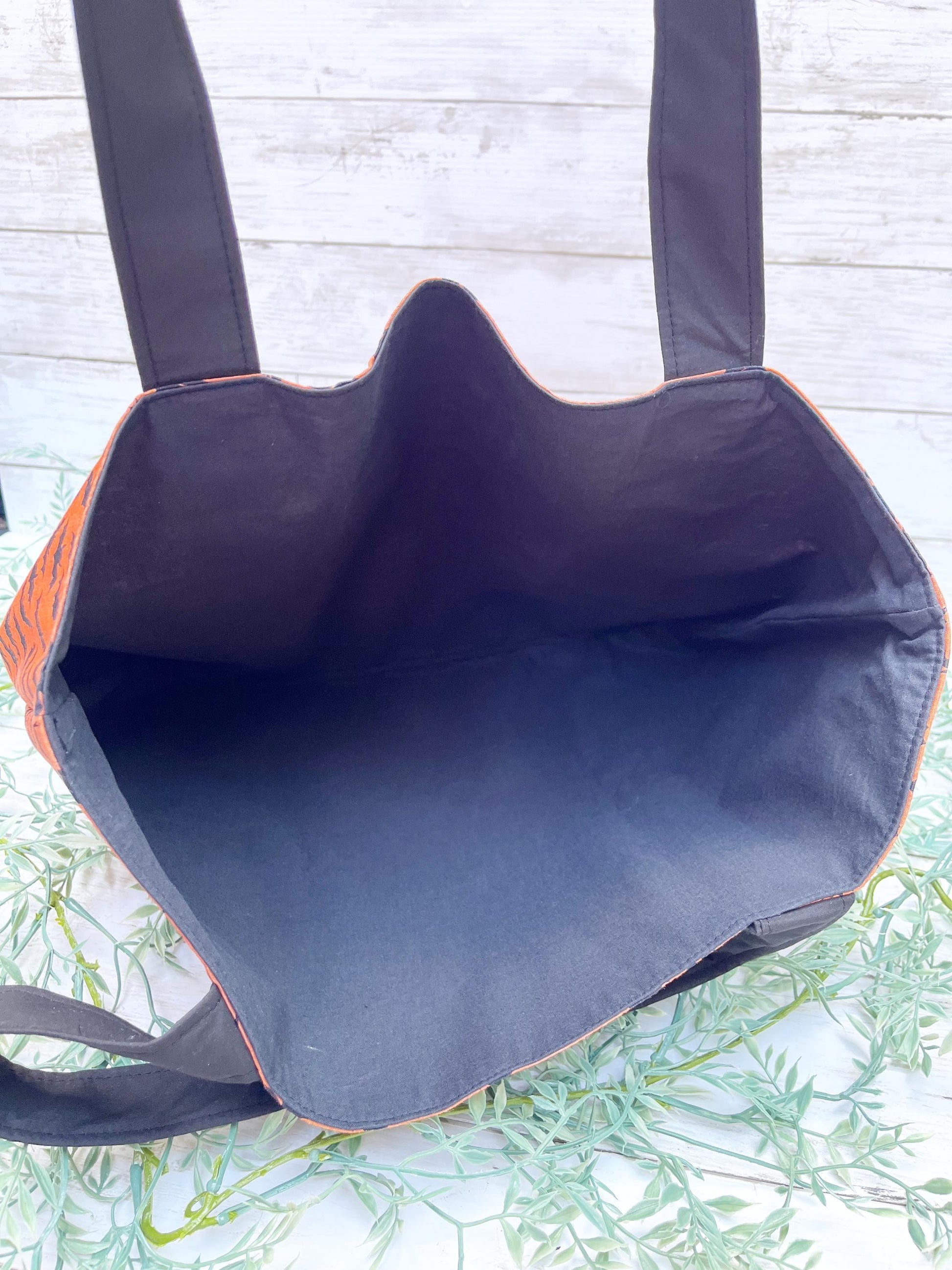 Black tote bag with black  interior lining on a light wooden surface.