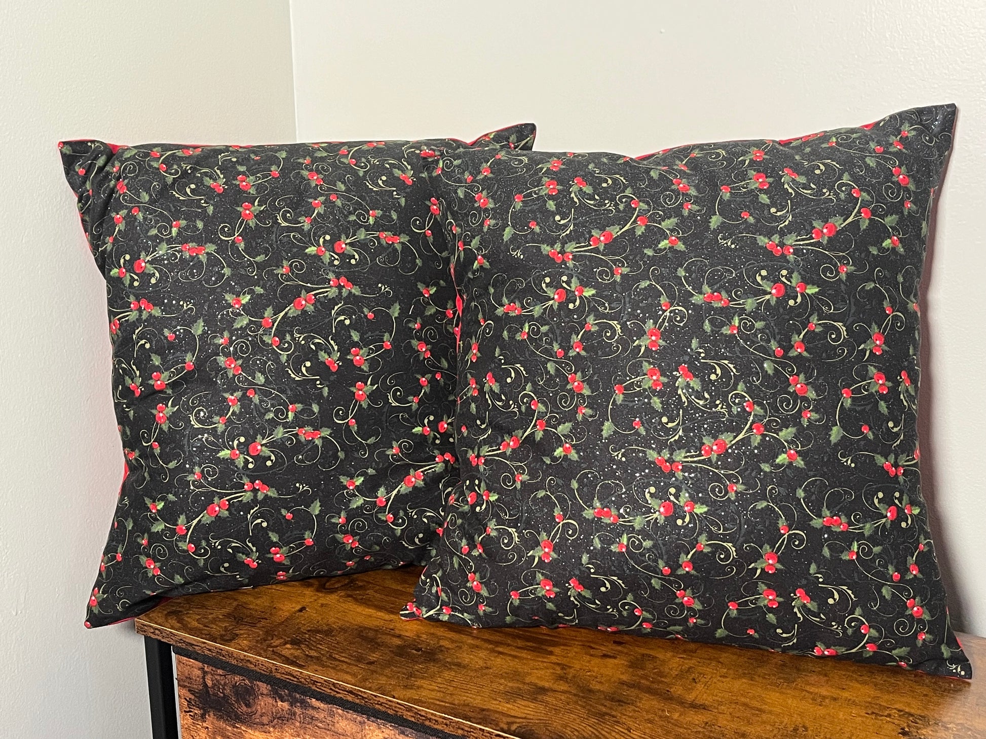 Two Holly themed  pillows on a wooden surface with a grey background
