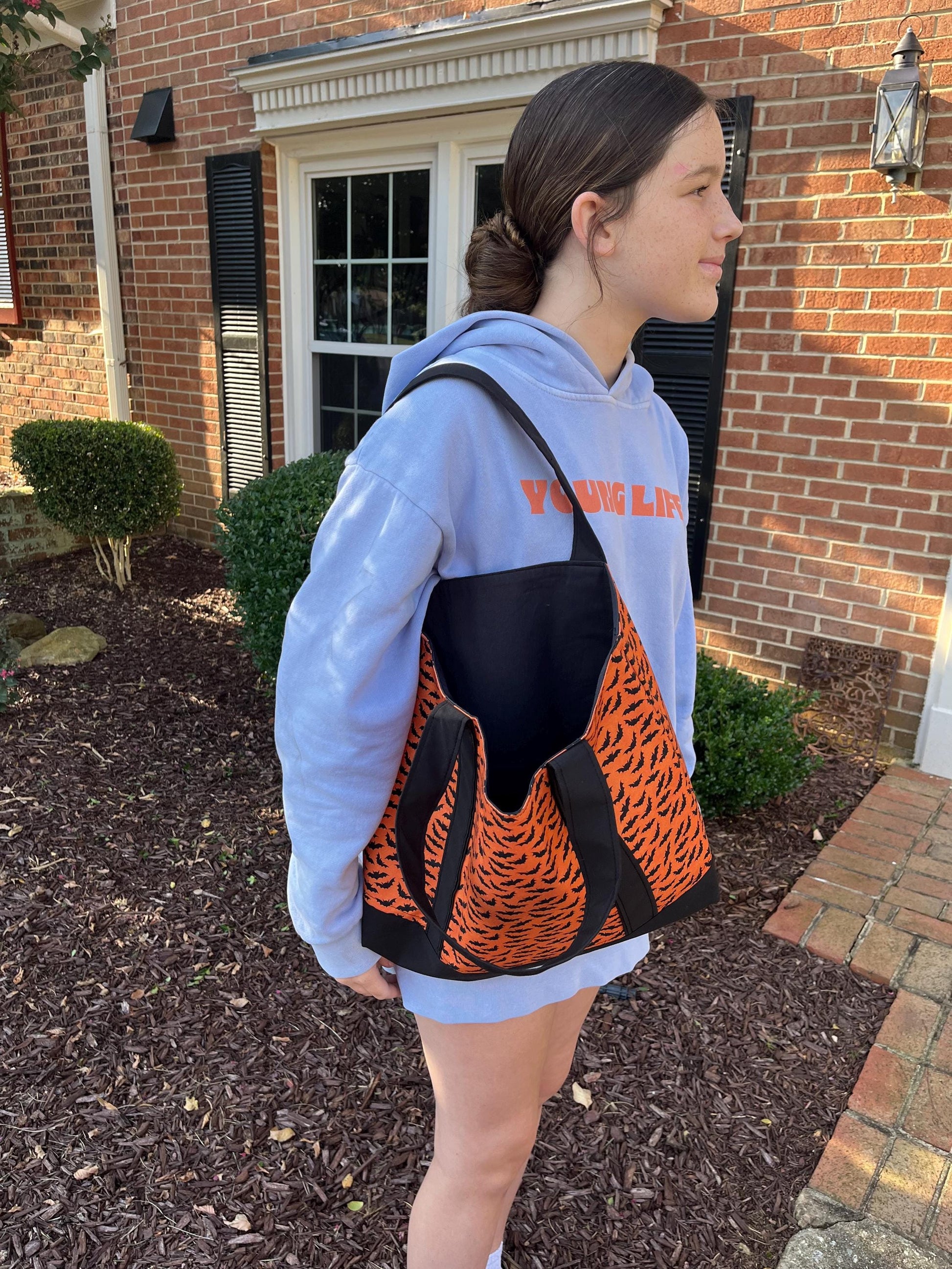 Person wearing a blue hoodie with 'Young Life' text, carrying an orange and black totebag outdoors.