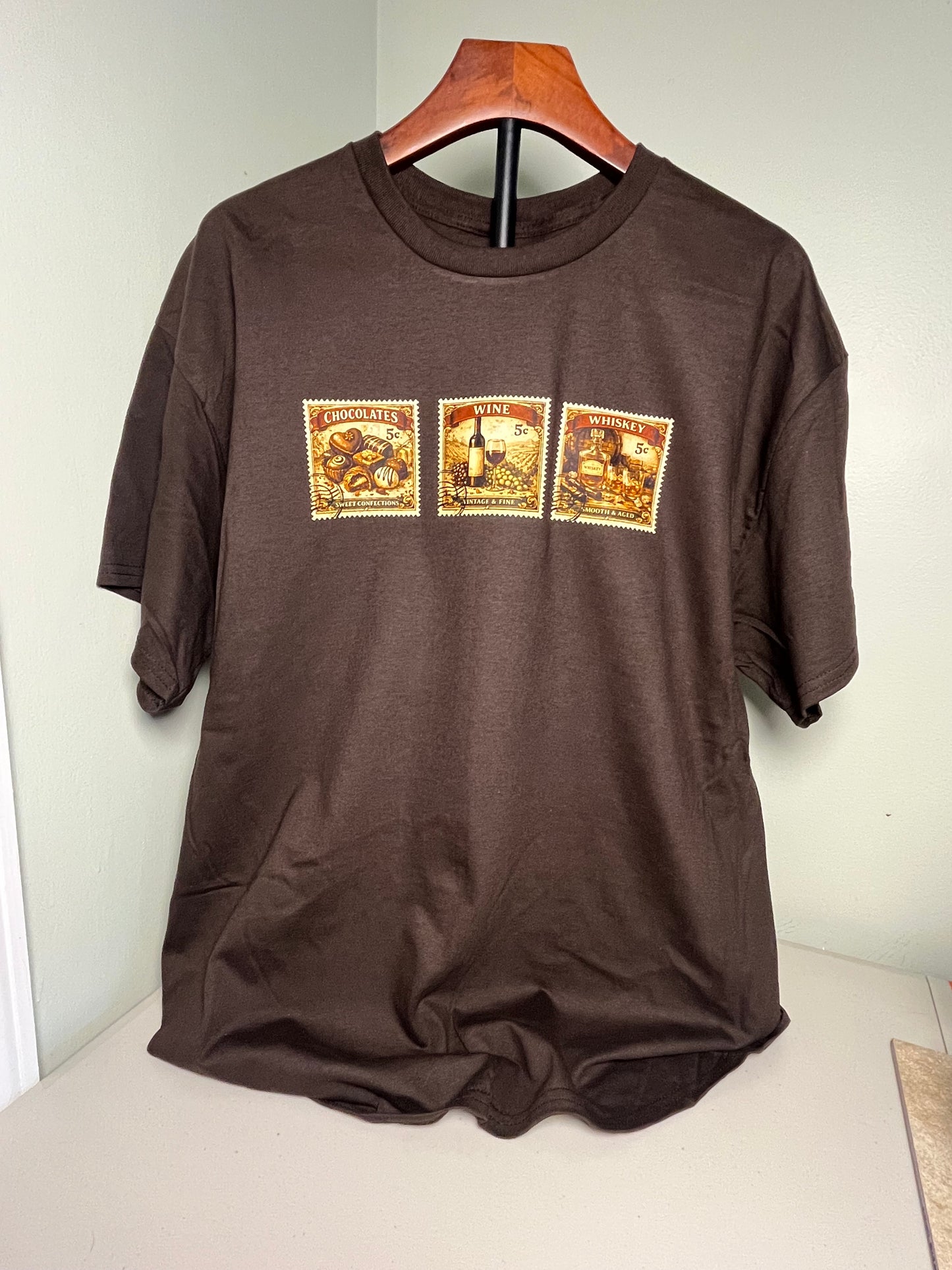 Brown short sleeve shirt with three vintage stamp theme graphics on front chest representing whiskey, wine and chocolate