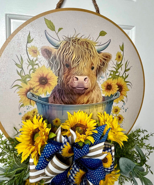Decorative door hanger with a Highland cow illustration, sunflowers, and a bow on a white background