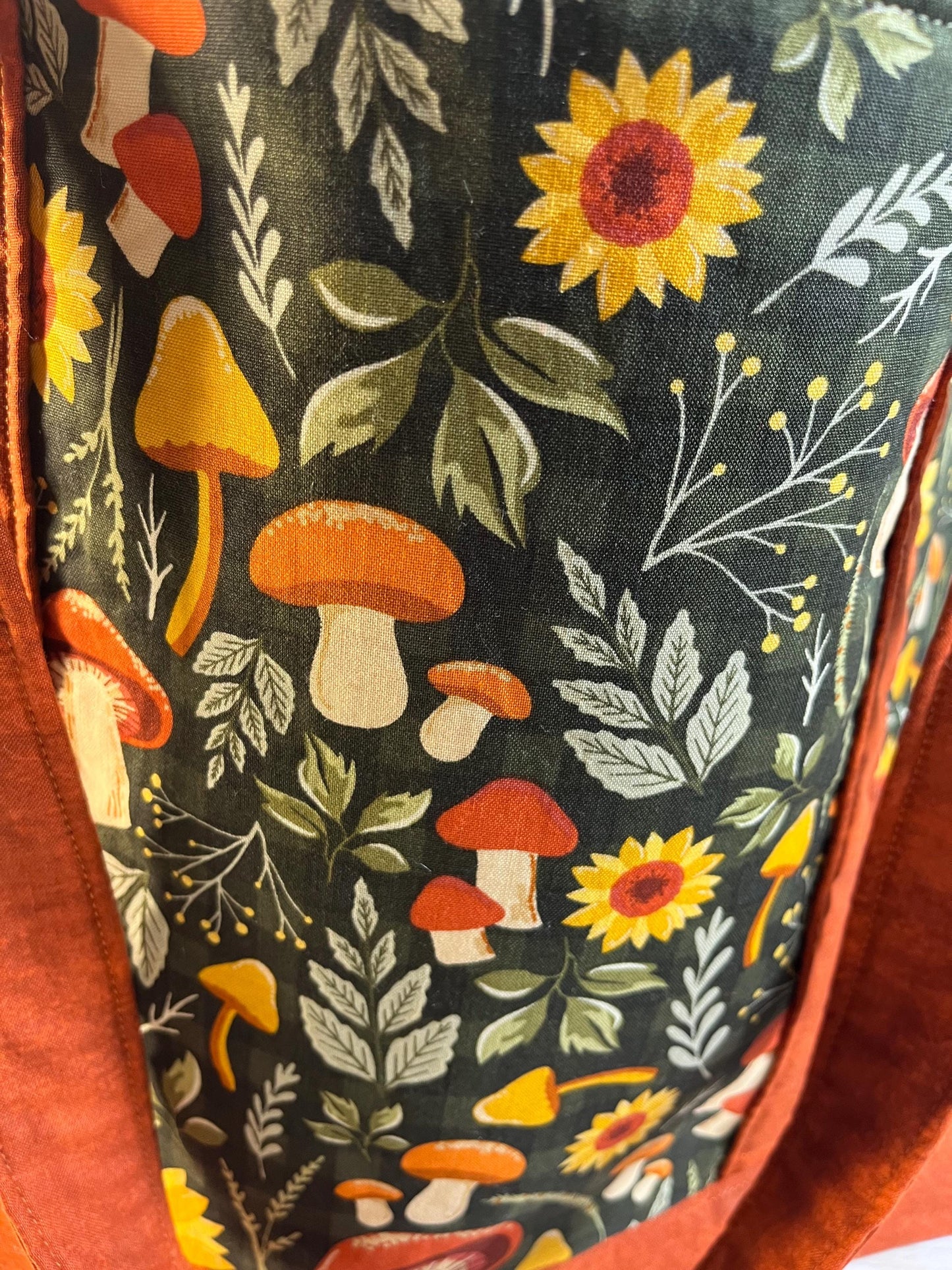 Close-up of a fabric with a nature-themed pattern featuring mushrooms and sunflowers on a dark background.