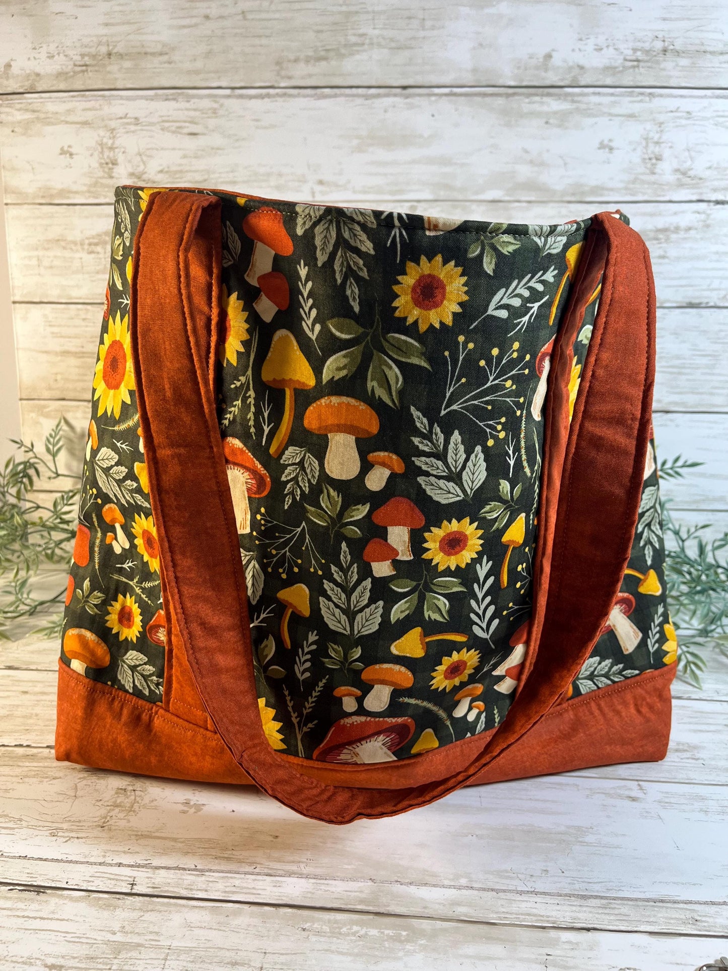 Tote bag with autumn-themed design featuring sunflowers and mushrooms on a wooden surface.