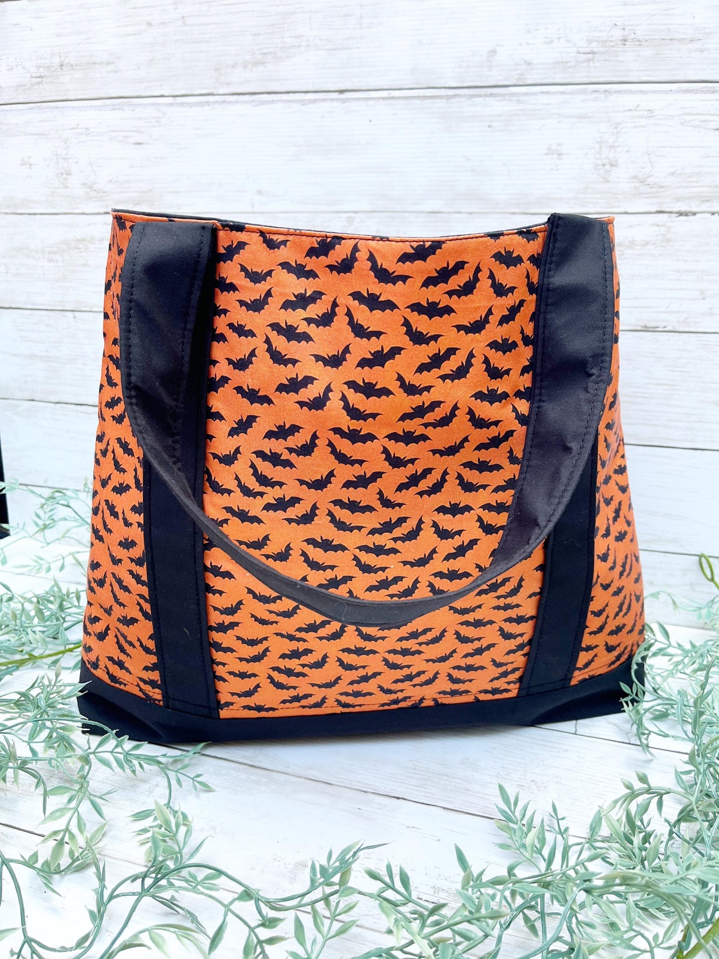 Orange tote bag with black bat pattern on a wooden surface