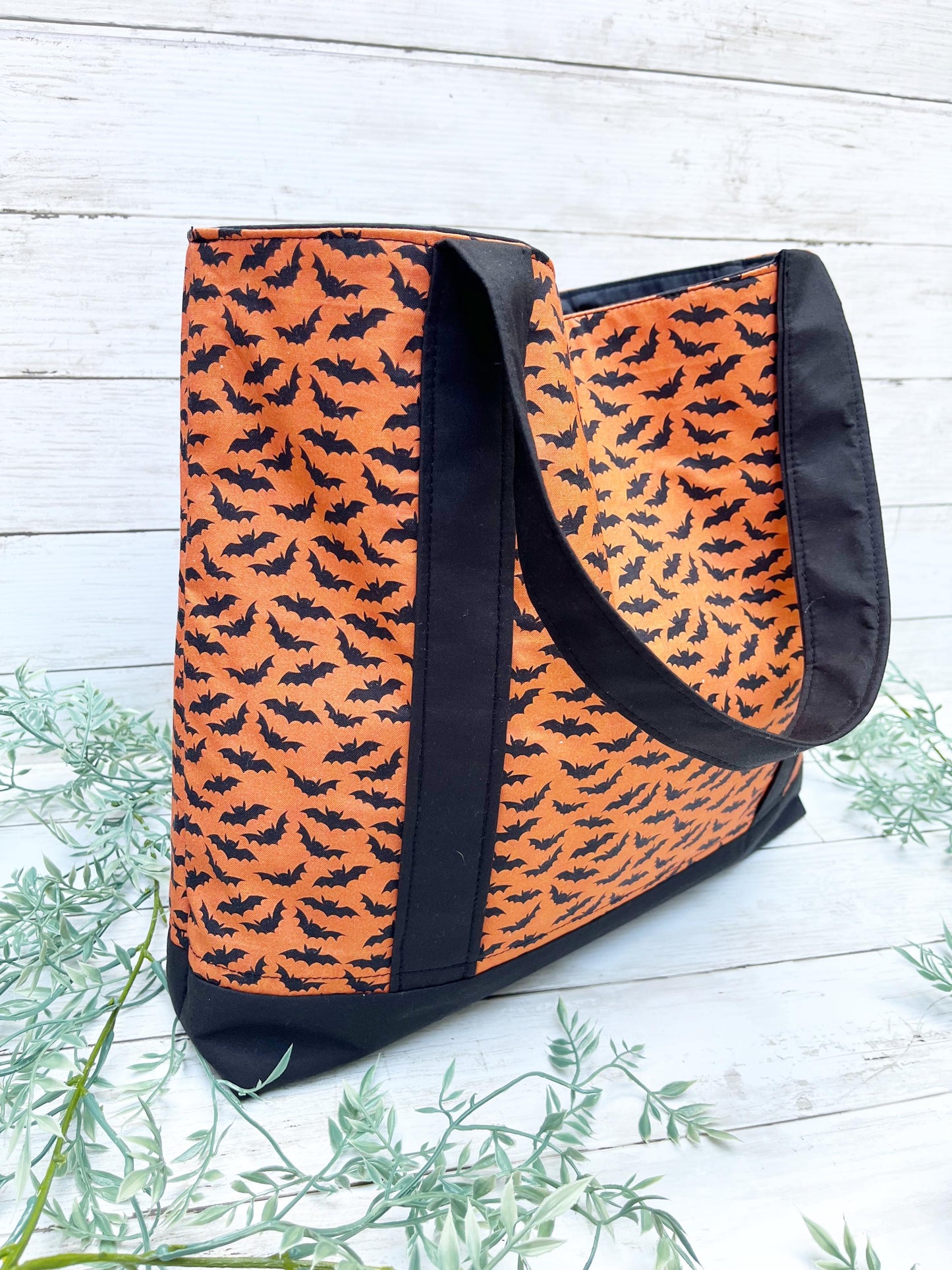 Orange tote bag with black bat pattern on a light wooden surface