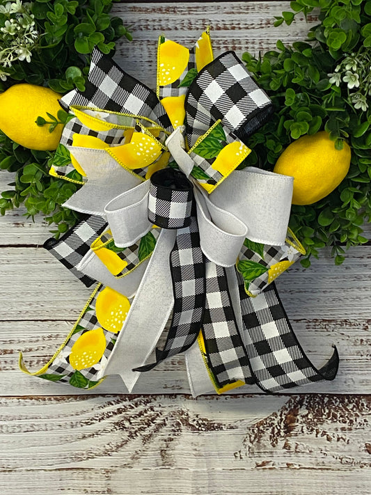 Decorative wreath with black and white checkered ribbon, yellow lemons, and greenery on a wooden surface.