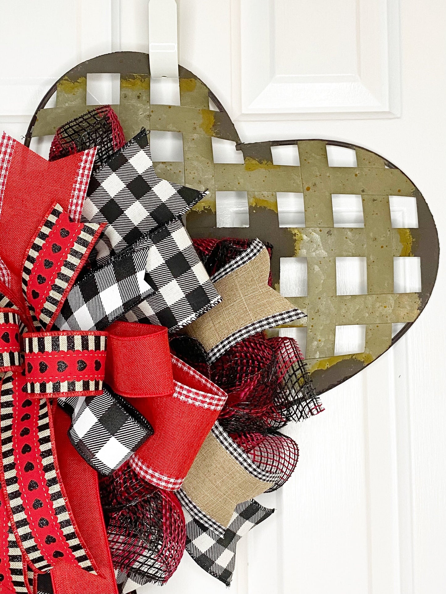 Heart-shaped decorative wreath with red, black, and plaid ribbons on a white door.